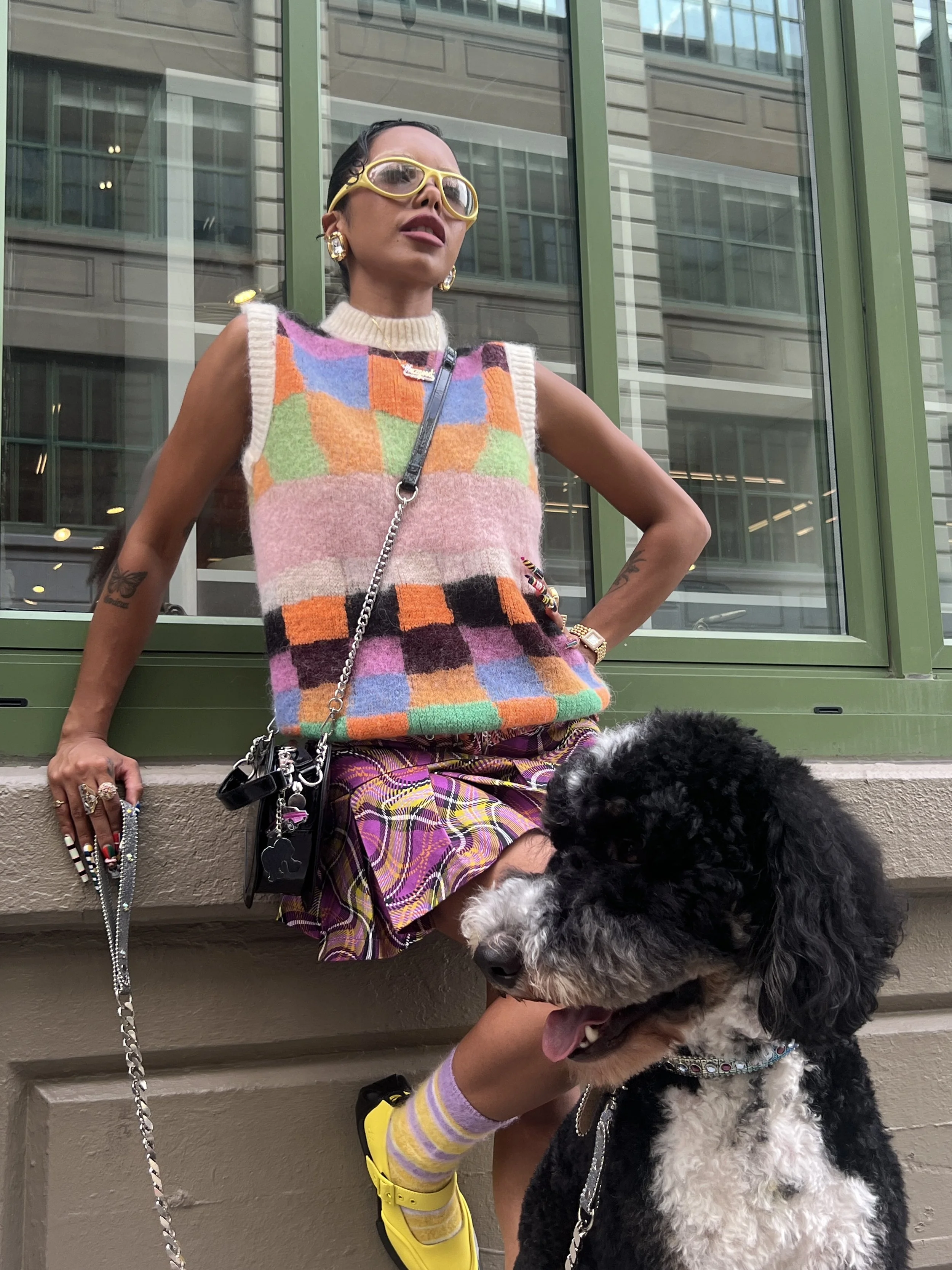 A woman with dark hair and glasses posing with a poodle dog outside a building with large glass windows.